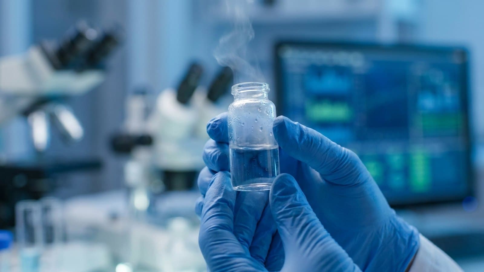 Gloved researcher's hands holding a vial of a clear personalized mRNA cancer-vaccine solution in a modern biotech laboratory, with out-of-focus lab instruments and screens showing genomic data in the background, representing Merck and Moderna's individualized neoantigen therapy.